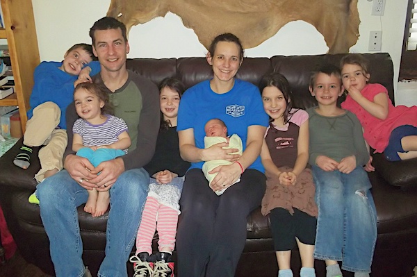 Beautiful Births family of nine on couch holding newborn baby after homebirth.