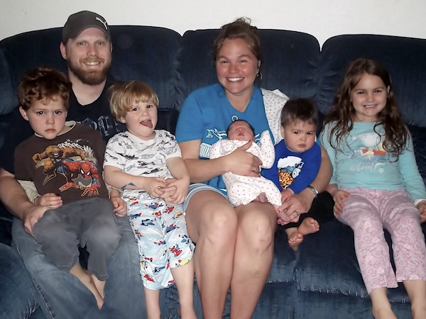 Beautiful Births family of seven on couch holding newborn baby after homebirth.