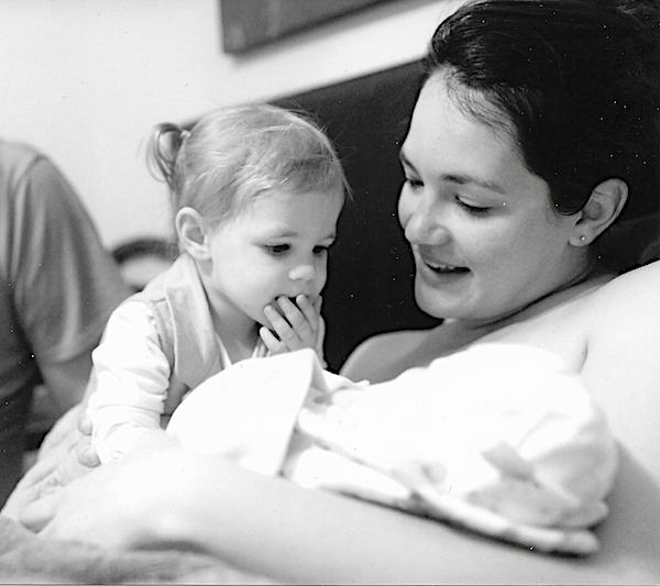 Beautiful Births mother and small child looking lovingly at new baby after homebirth.