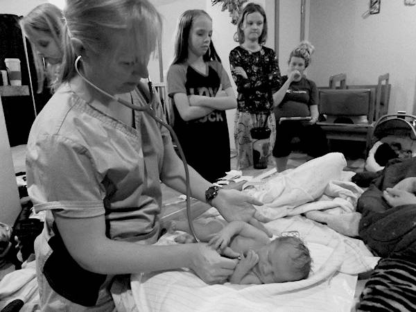 Tara Stephens, Midwife and Owner of Beautiful Births Homebirth Midwifery Practice in Colorado Springs, CO giving an infant a home baby wellness checkup with siblings looking on.