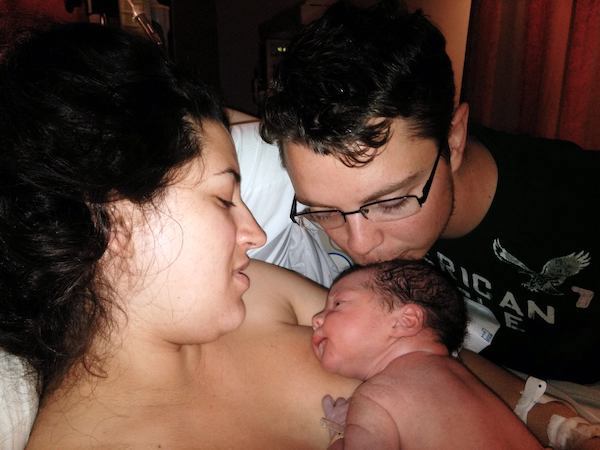 Couple holding and kissing head of newborn baby.